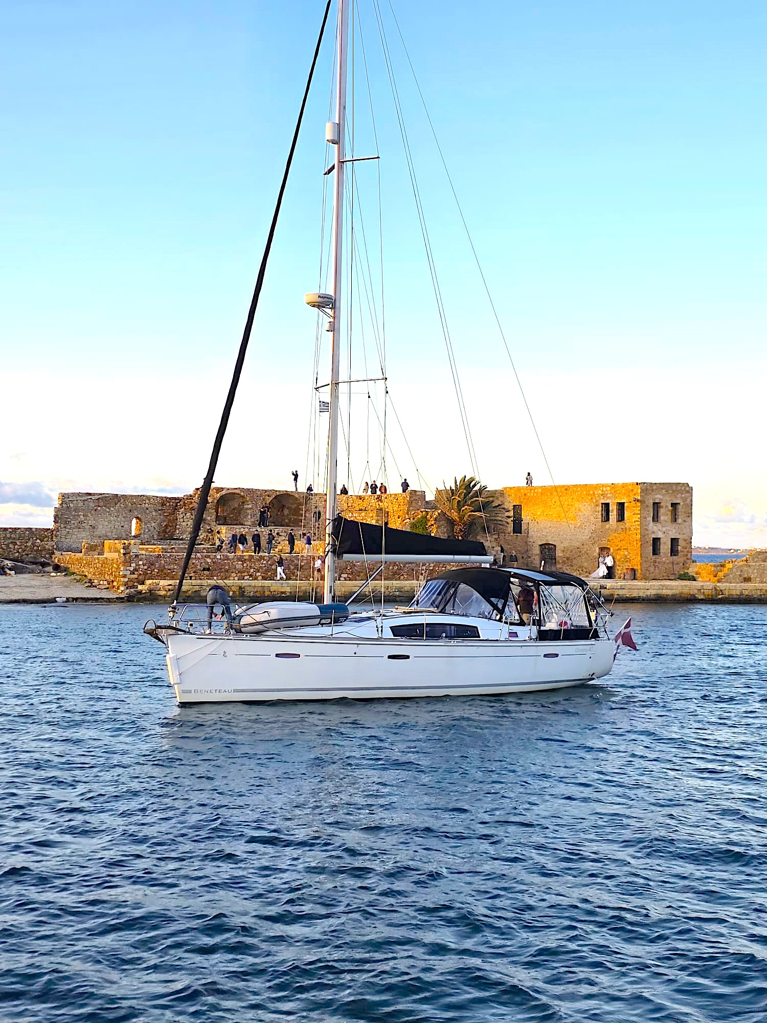 Topas sailing past a Mediterranean fortress at golden hour