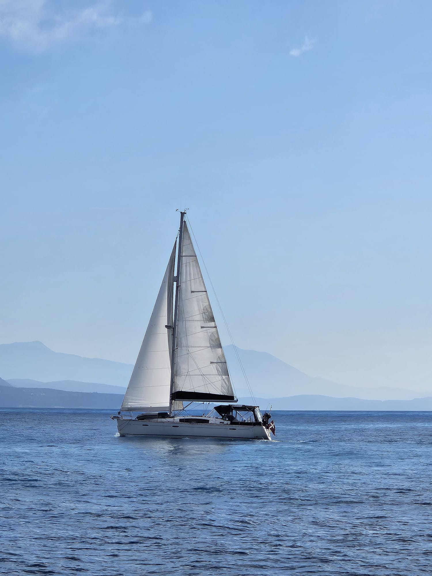 Topas under full sail with Danish flag flying, hazy mountains behind