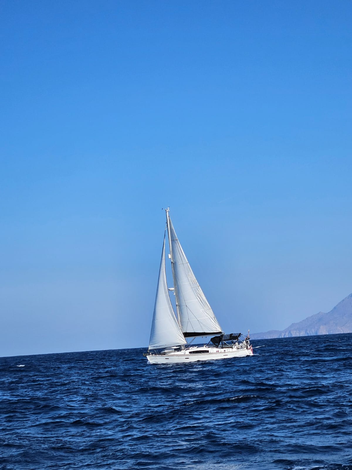 Topas sailing upwind on deep blue water along a mountainous coast